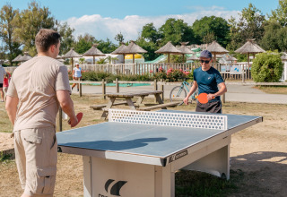 Zwei Männer spielen draußen Tischtennis an einem sonnigen Tag im Flower Camping Le Vorlen, Bretagne, Frankreich.