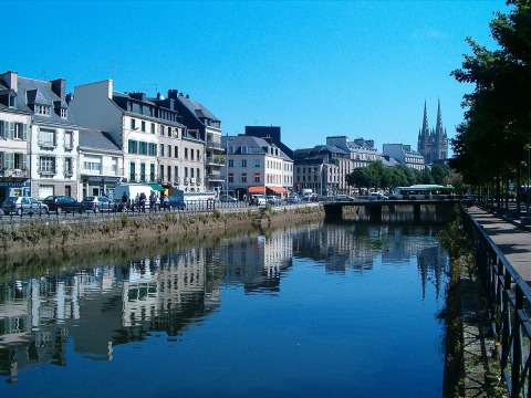 Billede af en kanal med refleksioner af huse i Fouesnant, Bretagne, Frankrig, med en kirke i baggrunden.