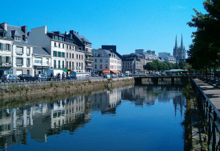View of a canal with reflections of houses in Fouesnant, Brittany, France, with a church spire in the background.