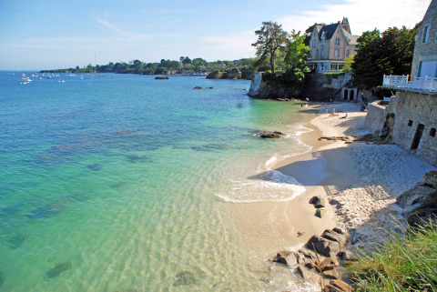 Scenic coastline near Fouesnant in Brittany, France, featuring clear blue water, sandy beach, and charming homes.