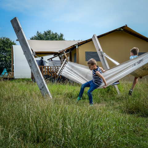 Zwei Kinder spielen auf einer Hängematte vor Zelten im Holiday Park Mölke, Overijssel, Niederlande.