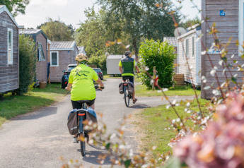 Dos personas montan en bicicleta entre casas móviles en Standard Wooden Mobile Home de Flower Camping Le Vorlen en Francia.