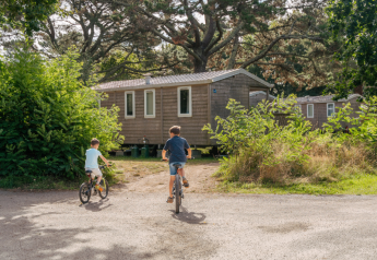 Due bambini vanno in bicicletta vicino a una casa mobile standard con 3 camere al Flower Camping Le Vorlen, Francia.