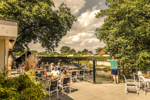 Terraza exterior en Holiday Park Mölke, Overijssel, Países Bajos, con personas disfrutando del sol y río.