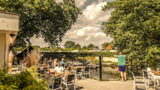 Terraza exterior en Holiday Park Mölke, Overijssel, Países Bajos, con personas disfrutando del sol y río.