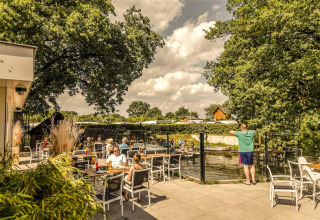 Buitenterras bij Holiday Park Mölke in Overijssel, Nederland, met mensen die eten en van de zon genieten.