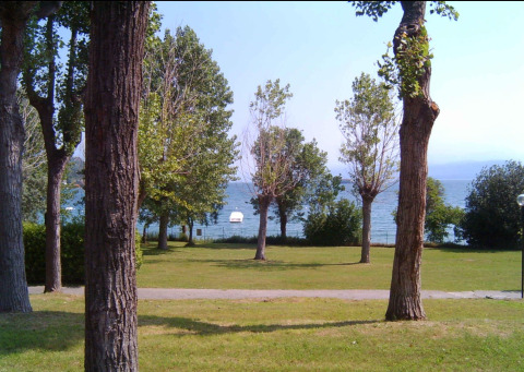 Vista de césped, árboles y el lago de Garda desde Sivinos Camping Boutique en Lombardía, Italia.