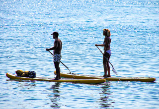Zwei Personen paddeln auf gelben Boards auf dem Wasser bei Manerba del Garda, Lombardei, Italien.