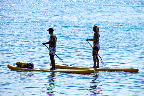 Two people paddleboarding on yellow boards in the sun near Manerba del Garda, Lombardy, Italy.