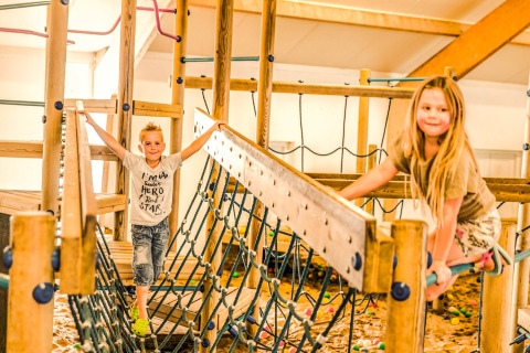 Dos niños juegan en un parque infantil interior con estructuras de madera y redes en Holiday Park Mölke, Países Bajos.