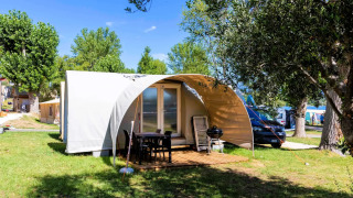 Das Safari-Zelt Coco Suite mit überdachter Terrasse, Grill und Möbeln, umgeben von Bäumen und Sonne.
