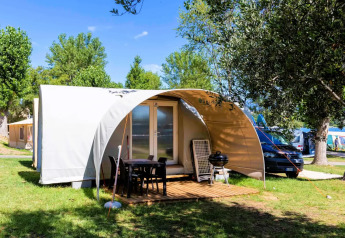 Coco Suite safaritent met schaduwterras, buitenmeubels en barbecue, tussen groene bomen in zonlicht.