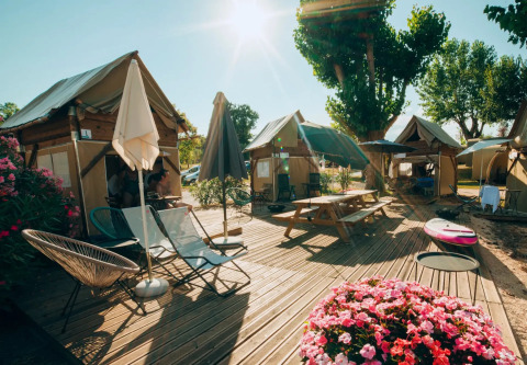 Safari tent Airstay met houten terras, bloembakken, tuinstoelen en parasols in de zonneschijn.