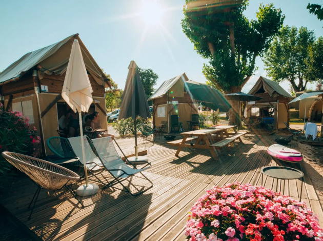 Safari tent Airstay met houten terras, kleurrijke bloemen, tuinmeubilair en parasols op een zonnige dag.
