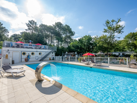 Piscina all'aperto con lettini e fontana al Flower Camping La Canadienne, Nouvelle-Aquitaine, Francia.