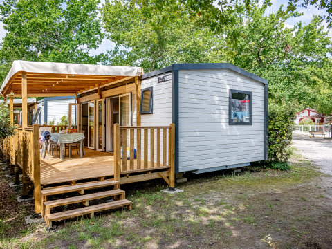 Stacaravan Premium 33m2 met houten terras, buitentafel en groen rondom op een gezellige campingplek.