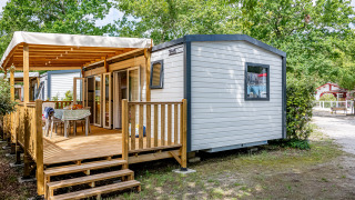 Stacaravan Premium 33m2 met houten terras, buitentafel en groen rondom op een gezellige campingplek.
