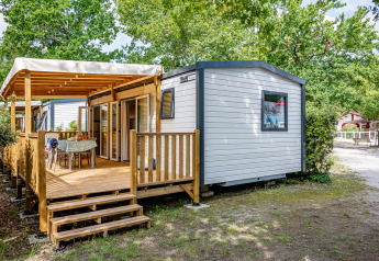 Stacaravan Premium 33m2 Mobilheim mit überdachter Holzterrasse, Sitzbereich und Bäumen im Campingplatz.