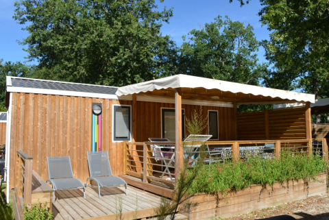 Cabaña de madera con terraza y tumbonas en Flower Camping La Canadienne, Nueva Aquitania, Francia.