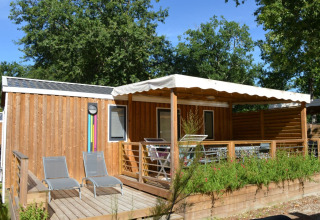 Cabaña de madera con terraza y tumbonas en Flower Camping La Canadienne, Nueva Aquitania, Francia.