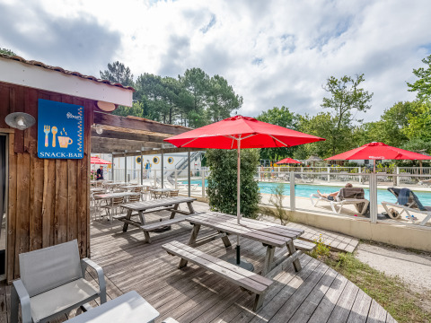 Zona de piscina exterior en Flower Camping La Canadienne con sombrillas rojas, mesas y cartel de snack-bar.