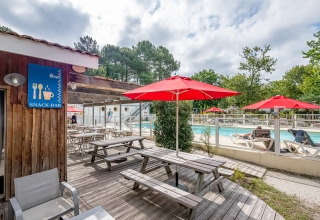 Area piscina esterna al Flower Camping La Canadienne con ombrelloni rossi, tavoli e insegna snack-bar.