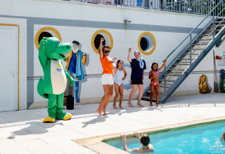 Children and adults dance by the pool with a crocodile mascot at Flower Camping La Canadienne in France.