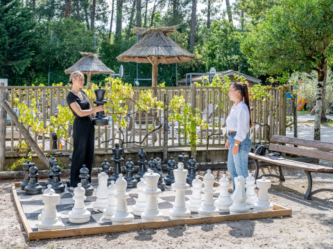 Zwei Frauen spielen mit übergroßen Schachfiguren im Freien im Flower Camping La Canadienne, Frankreich.