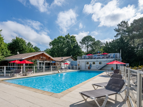 Schwimmbad mit Liegestühlen und roten Sonnenschirmen bei Flower Camping La Canadienne in Nouvelle-Aquitaine.