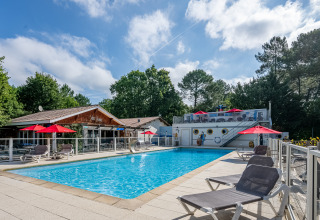Schwimmbad mit Liegestühlen und roten Sonnenschirmen bei Flower Camping La Canadienne in Nouvelle-Aquitaine.
