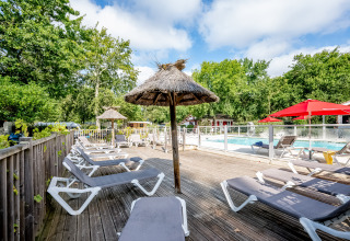Sonnige Liegestühle und Strohdach-Sonnenschirme am Pool von Flower Camping La Canadienne, Nouvelle-Aquitaine.