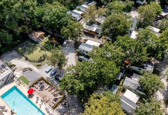 Aerial view of Flower Camping La Canadienne with pool, playground, mobile homes, and abundant trees.