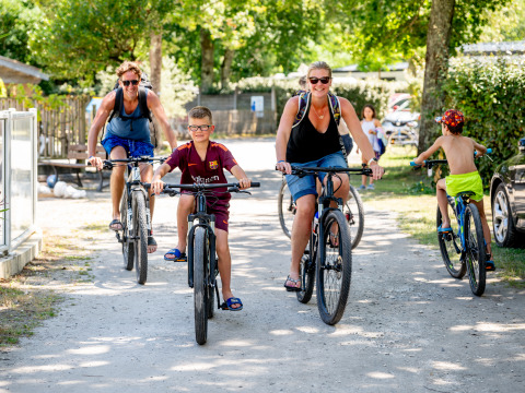 Familie cykler sammen på en solrig sti i Flower Camping La Canadienne, Nouvelle-Aquitaine, Frankrig.