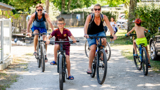 Gezin fietst samen over zonnig pad bij Flower Camping La Canadienne, Nouvelle-Aquitaine, Frankrijk.