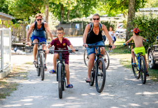 Gezin fietst samen over zonnig pad bij Flower Camping La Canadienne, Nouvelle-Aquitaine, Frankrijk.