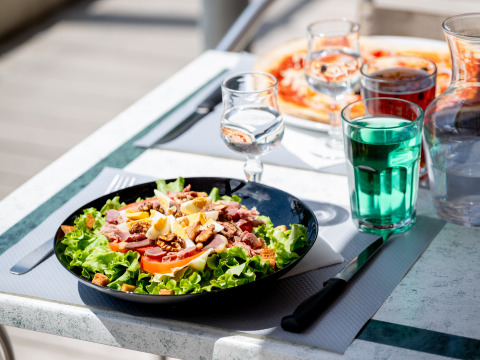 Udendørs bord med frisk salat, grøn drik og vandglas på Flower Camping La Canadienne, Nouvelle-Aquitaine, Frankrig.