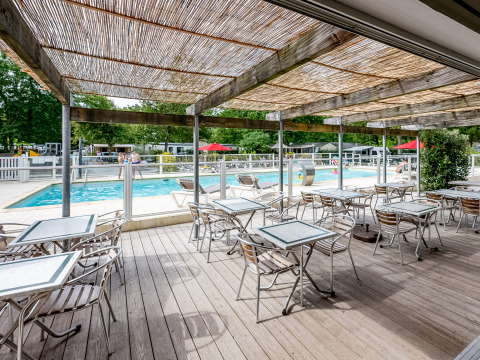 Außenterrasse mit Tischen und Blick auf den Pool im Flower Camping La Canadienne, Nouvelle-Aquitaine, Frankreich.