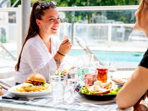 Twee vrouwen genieten van een lunch buiten bij het zwembad op Flower Camping La Canadienne in Frankrijk.