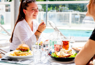 Zwei Frauen genießen ein Mittagessen im Freien am Pool im Flower Camping La Canadienne in Frankreich.