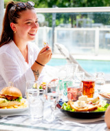 Twee vrouwen genieten van een lunch buiten bij het zwembad op Flower Camping La Canadienne in Frankrijk.