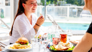 Twee vrouwen genieten van een lunch buiten bij het zwembad op Flower Camping La Canadienne in Frankrijk.