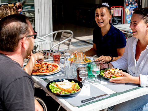 Gruppe venner nyder pizza og salat udendørs på Flower Camping La Canadienne i Nouvelle-Aquitaine, Frankrig.