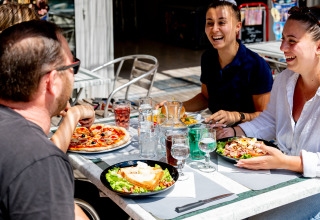 Grupo de amigos disfruta de pizza y ensalada al aire libre en Flower Camping La Canadienne en Nouvelle-Aquitaine, Francia.