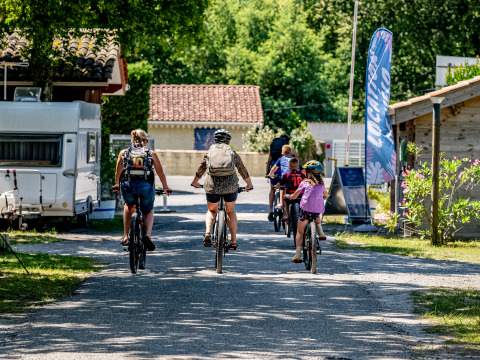 Families ride bicycles through Flower Camping La Canadienne holiday park in Nouvelle-Aquitaine, France.