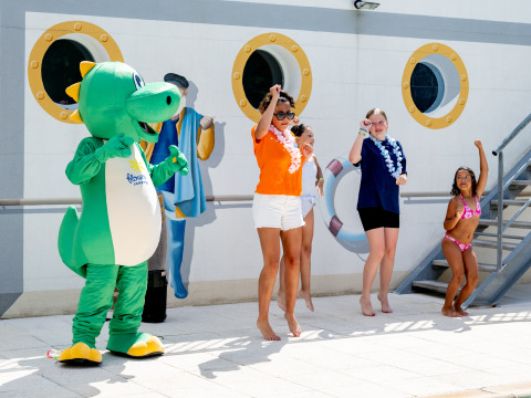 Bambini e adulti ballano con una mascotte verde al Flower Camping La Canadienne in Nouvelle-Aquitaine, Francia.