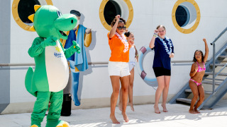 Kinderen en volwassenen dansen met een groene mascotte bij Flower Camping La Canadienne in Nouvelle-Aquitaine, Frankrijk.