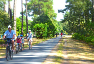 En familie cykler på en skovsti i solskin ved Flower Camping La Canadienne, Nouvelle-Aquitaine, Frankrig.