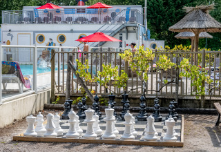 Ajedrez gigante al aire libre junto a la piscina en Flower Camping La Canadienne, Nouvelle-Aquitaine, con huéspedes cerca.