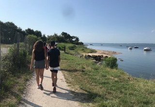 Persone che camminano su un sentiero vicino all'acqua ad Arès, Nouvelle-Aquitaine, Francia, in una giornata soleggiata.