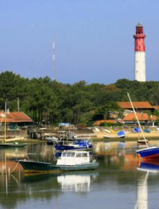 Kustscène nabij Arès in Nouvelle-Aquitaine, Frankrijk, met boten, huizen en een vuurtoren op de achtergrond.